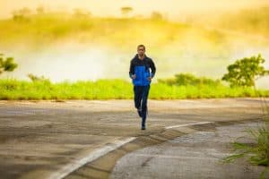 image of a man in a black/blue jacket and black track pants running at the side of the road during sunrise