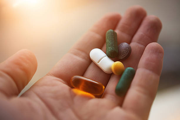 A hand holding a selection of dietary supplements, illuminated by warm sunlight.