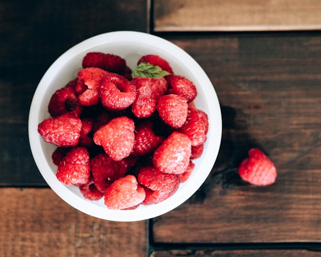 A bowl full of fresh, vibrant raspberries on a wooden background