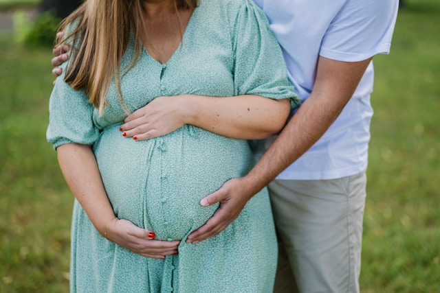 A pregnant woman in a green dress with a man's hands around her, both preparing for IVF.
