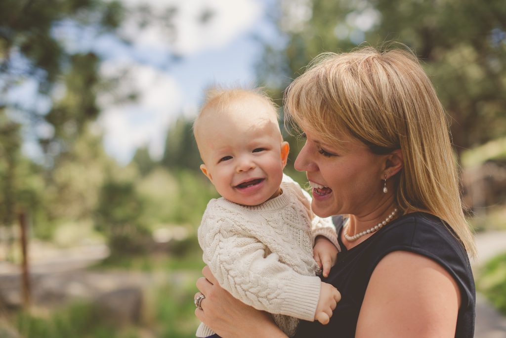 A joyful woman in her mid-forties holding a laughing baby boy in a cozy knitted sweater.