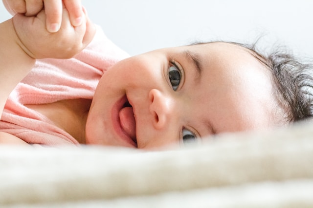 A joyful baby with sparkling eyes and a tiny smile, grasping an adult's finger with a tiny hand.