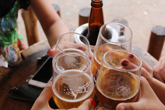 A close-up of four hands toasting with glasses of beer.