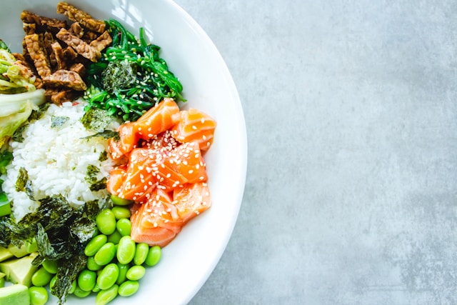 A fresh, colorful bowl of salmon poke with greens, rice, and edamame.