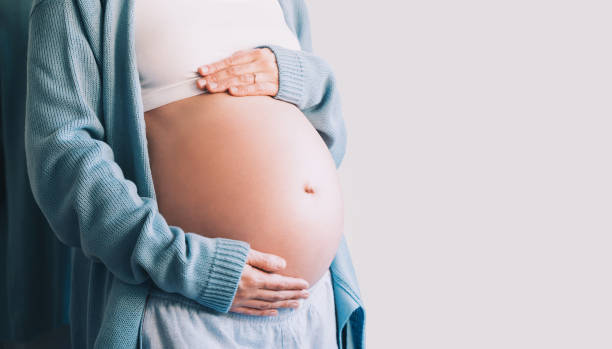 Pregnant person gently cradling their belly with both hands.
