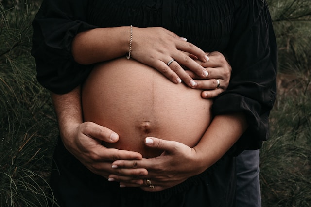 Close-up of a pregnant belly embraced by a couple's hands against a natural backdrop.
