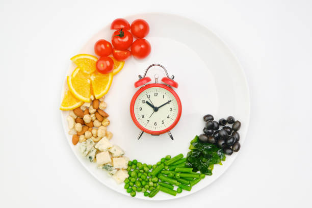 A creative presentation of healthy foods arranged on a plate to resemble a clock face, featuring tomatoes, oranges, chickpeas, and green vegetables.