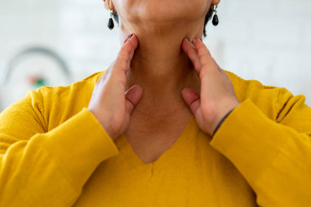 Woman touching her neck, indicating thyroid area, while wearing a yellow sweater.