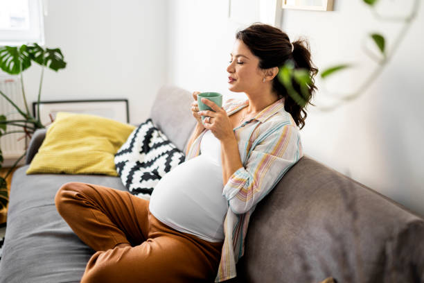 Pregnant woman relaxing on a couch at home, enjoying a cup of tea.