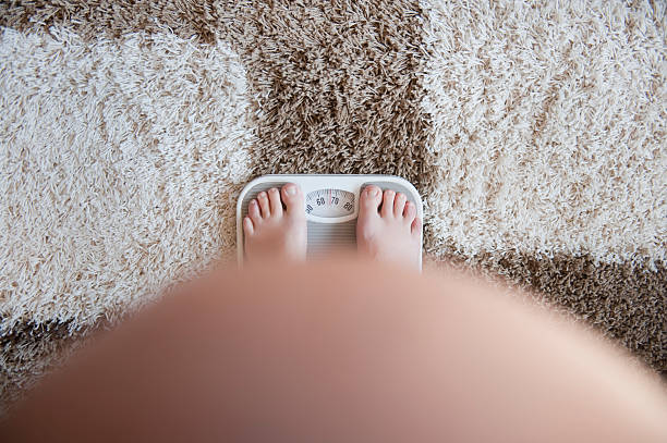 A pregnant woman standing on a scale, checking her weight at home.