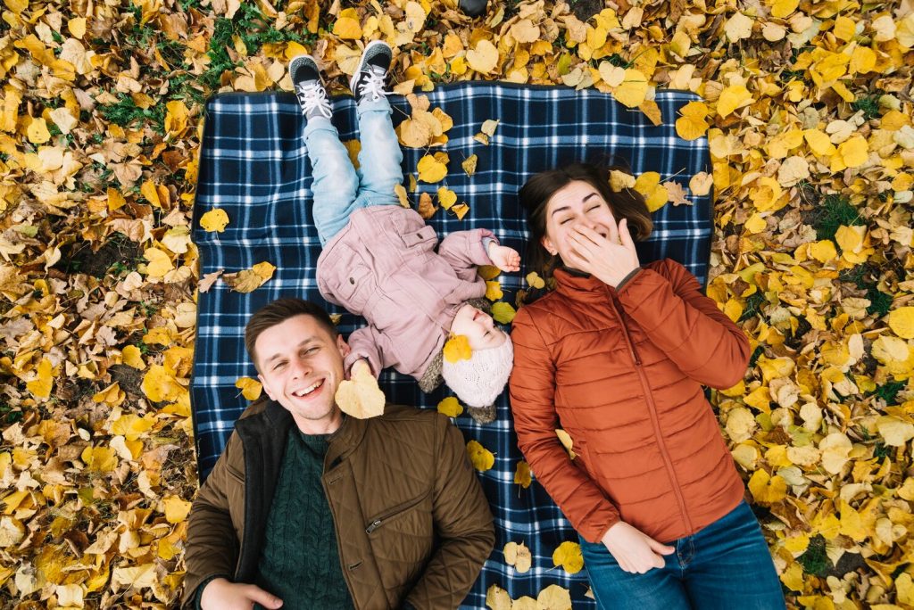 A happy family lying on a blanket surrounded by yellow autumn leaves, symbolizing joy and connection during the season of letting go.