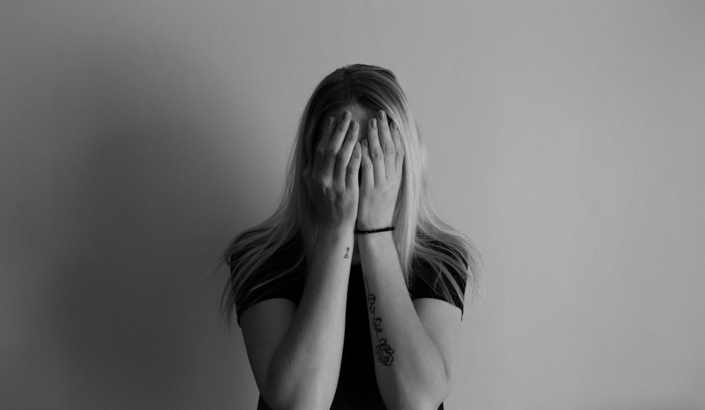 Grayscale photo of a woman covering her face with her hands, expressing emotional distress—used to illustrate the emotional impact of fertility complications in women.